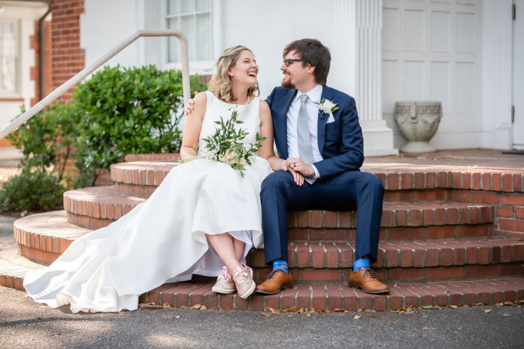 Newly married couple sitting next to each other on brick stairs laughing at a joke at The Solarium at Historic Scottish Rite in Decatur, GA