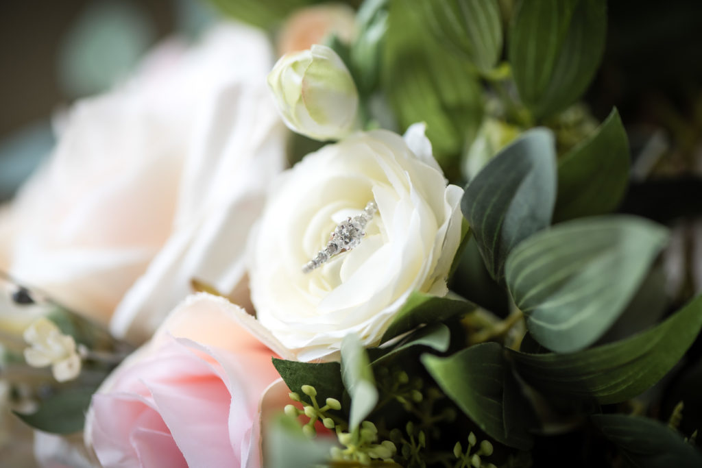 Photo of the bride's engagement ring on a white flower within the bridal bouquet