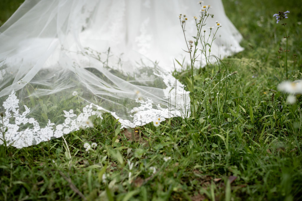 Close up of the bottom of the wedding dress as it rests on green grass