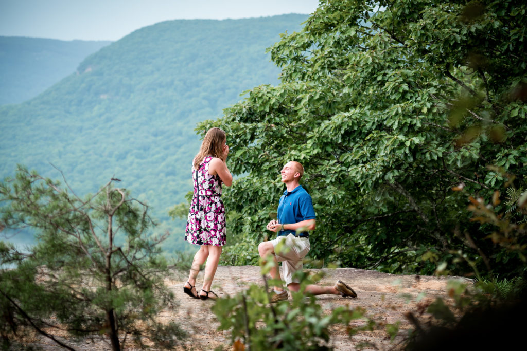 Girl putting hands to her face as boyfriend proposes to her on a mountaintop outside of Chattanooga TN