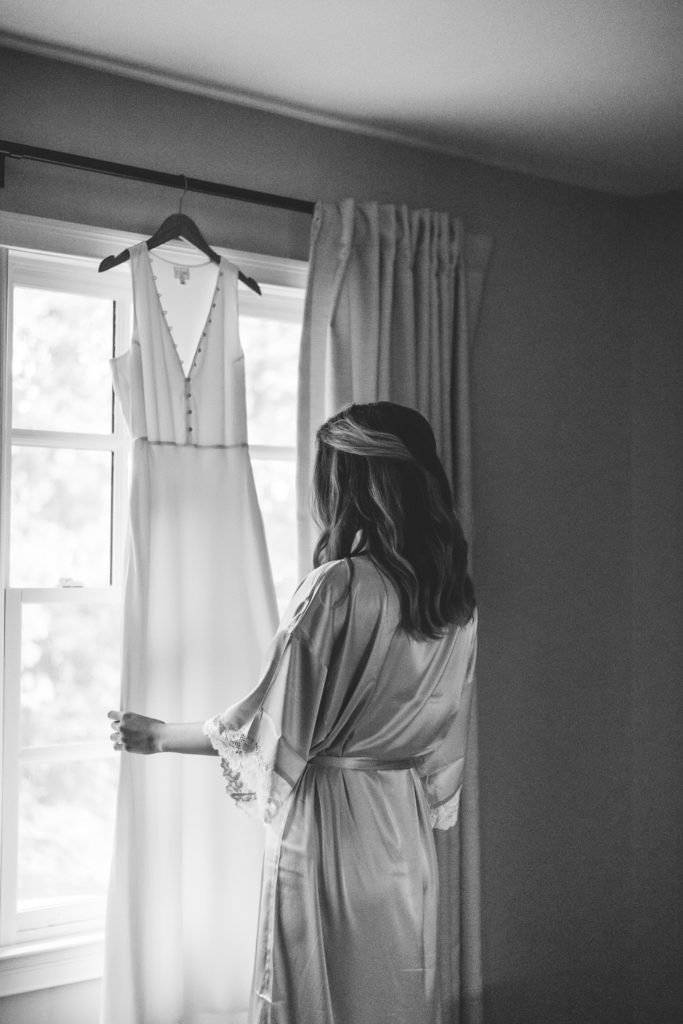 Bride gazing at wedding dress hanging on the window at intimate, backyard wedding in Marietta GA