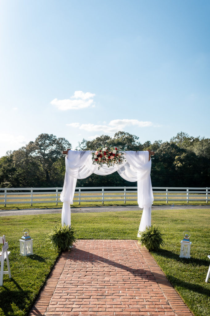 Photo of arbor with white drapery and maroon and green florals at wedding at The Gavi Estate and Barn in Forsyth GA