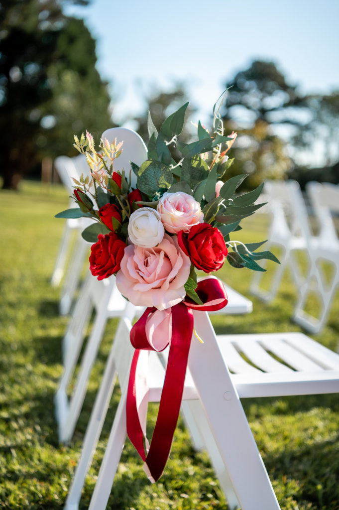 Photo of red, pink and white florals with greenery on ceremony chair at wedding at The Gavi Estate and Barn in Forsyth GA