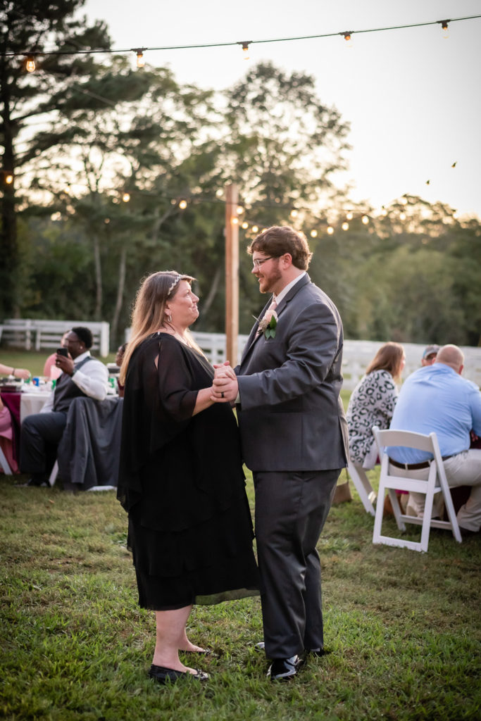 Groom and mother of the groom dancing outside under twinkling lights at wedding at The Gavi Estate and Barn in Forsyth GA