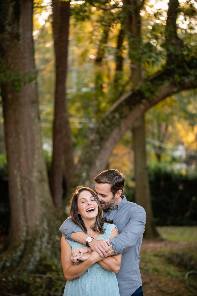 guy hugging his fiance from behind in the woods during golden hour