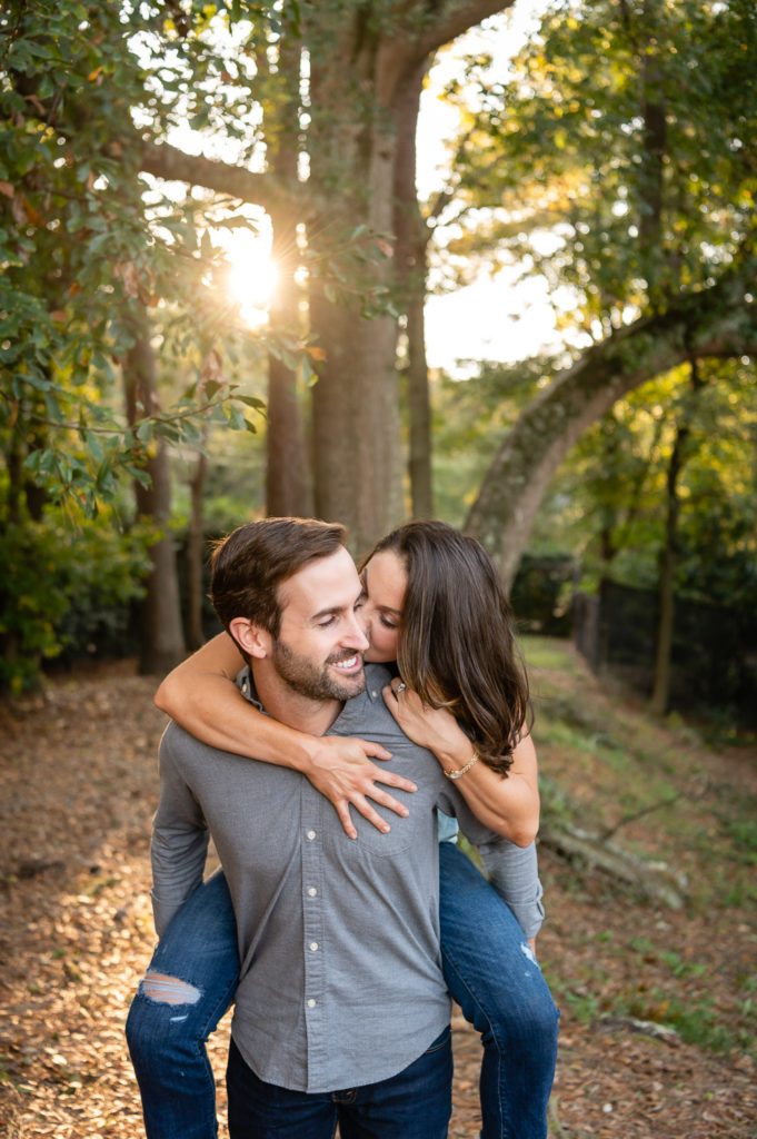 girl riding piggy back on fiance's back in the woods during golden hour