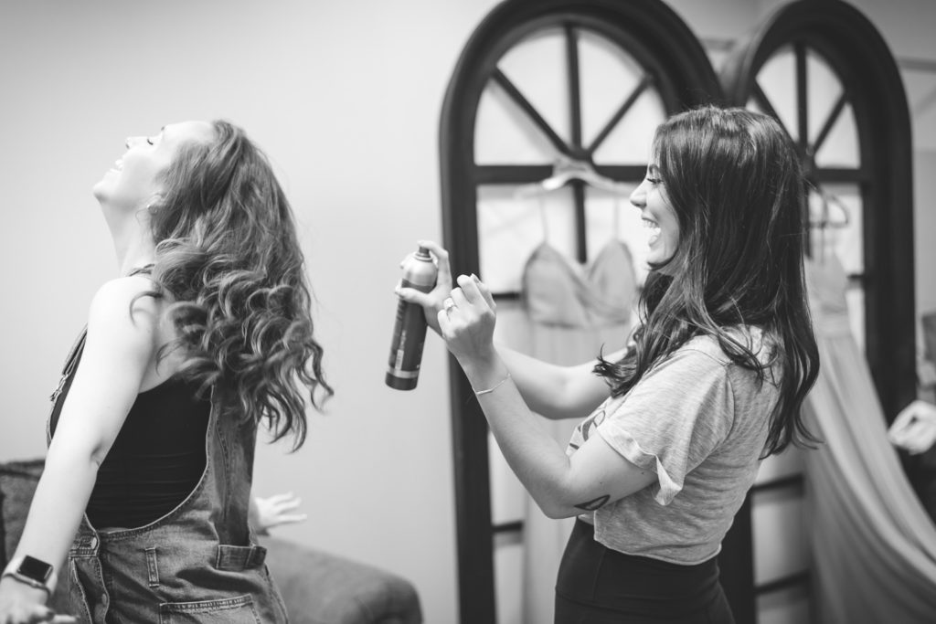 bridesmaid spraying bridesmaids hair with hairspray on the wedding day at The Hudgens Center for Art and Learning in Atlanta Georgia